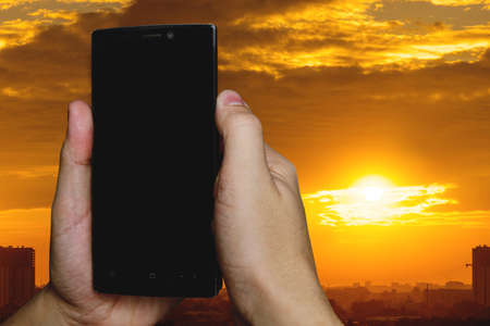 man using a touch screen smart phone hands in sunset sky on blurred urban city as background, vintage colorsの写真素材