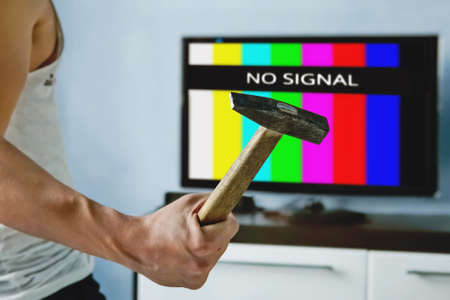 viewer is furious with the problems with broadcasting. Multi-colored stripes on the TV screen. The inscription on the TV NO SIGNAL. televiewer wants to smash the monitor with a hammer.の写真素材