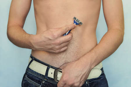 Male depilation. A man shaves his belly razors. Young attractive man using razor to remove hair from his body. epilation Bushの写真素材