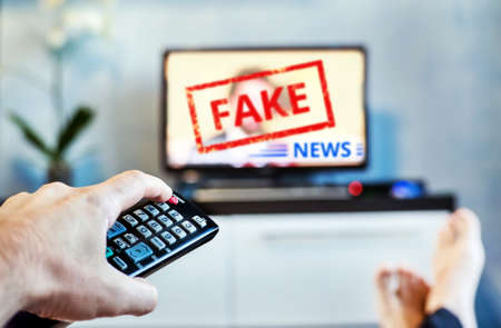 Fake News Propaganda HOAX Political TV Internet Social. young man watching the fake news report on TV at home. Agitation and propaganda in the modern television. switching channel on remote controlの写真素材