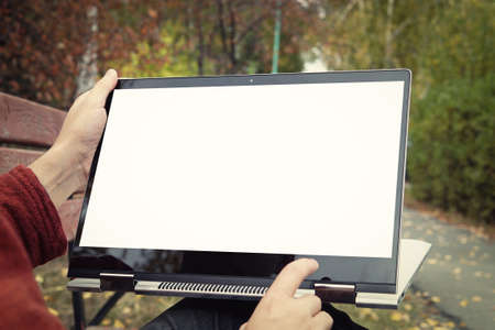 casual man sitting on a bench in the autumn Park with his legs crossed and presenting his laptop...