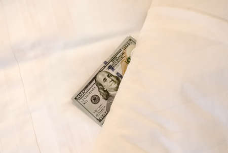 A tip on the bed. a hundred dollars under the blanket. payment for the services of prostitutes. Tips at the bed for the housekeeper in hotel.の写真素材