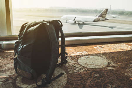 Silhouette of luggage or suitcase placed at the window at waiting terminal in international airports with airplan taking off behide the building. Forgotten Luggage. Lost hand Luggage. travel conceptの写真素材