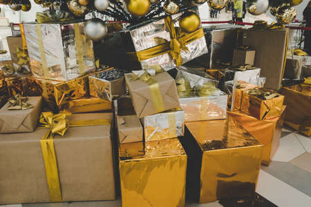 Golden gift box with ribbon under Christmas tree at living room. Gift in shiny gold packaging lying on the floor under the treeの写真素材