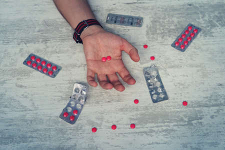 Close up of overdose pills and addict on the hands of men, The man committing suicide by overdosing on medication. red tablets in the hand of a young manの写真素材