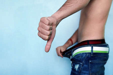 Finger down as a sign of bad potency. Man keeps his swimming trunks and jeans open looking at his...