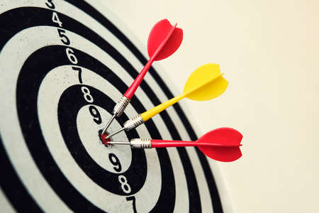 Side view of a dartboard with three darts in the bull's eye. Well-aimed dart throwing. Triple...