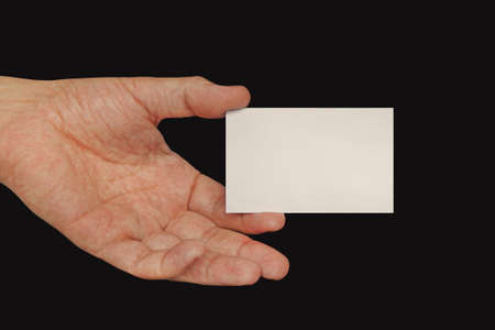 Closeup of male hand holding a blank white business card towards you. Over black background. White business card in male hand isolated on black backgroundの写真素材