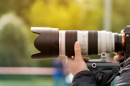 Handshot of a professional photographer outdoors. Man holds a modern camera device. Cameraman shoots...