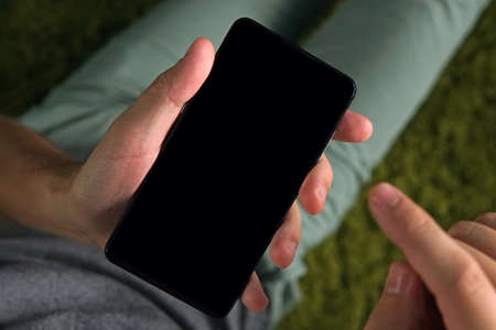Close up of a young man using the smartphone with the white screen. Person is on-line from a...