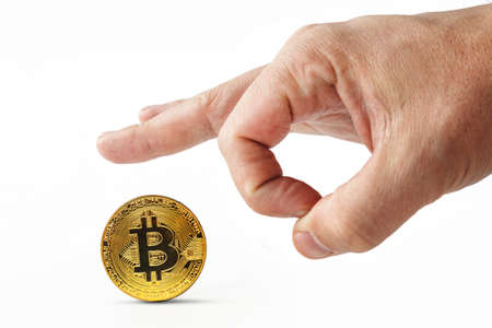 Male fingers push golden bitcoin away on a white background. Isolated mans hand throwing worthless cryptocoin away. Crash of cryptocurrency. Virtual money is depreciated. Useless bitcoins are kicked.の写真素材