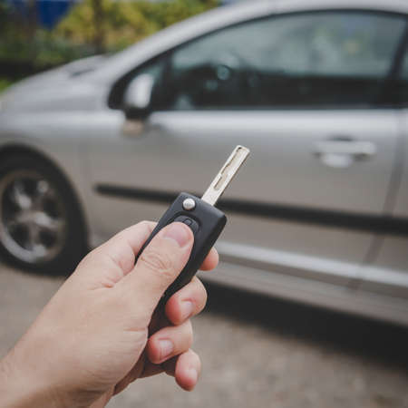 Man opens his car door with the control remote key. Male hand presses on the vehicle remote control alarm system on parked car background. Turning off automotive alarm. Close up of vehicular keyの写真素材