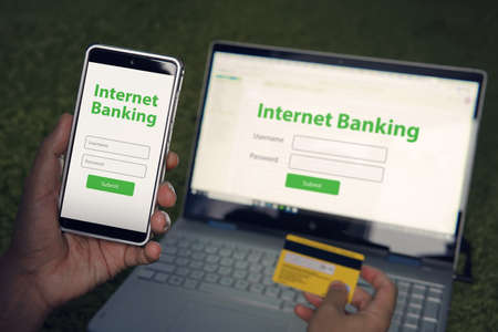 Man browsed homepage of internet banking service on his smartphone and laptop holding credit card. Online payment mobile banking concept. Written words Internet banking on phone and notebook screens.の写真素材