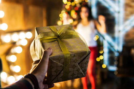 guy gives his girlfriend a gift for Christmas or new year. Box in Golden foil closeup on a background of jubilant happiness womenの写真素材