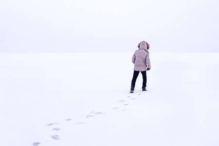 Man walking on snow, footprints in snow, behind. Cold Siberian winter. Russia. The guy in the winter jacket with a hood. white down jacketの写真素材