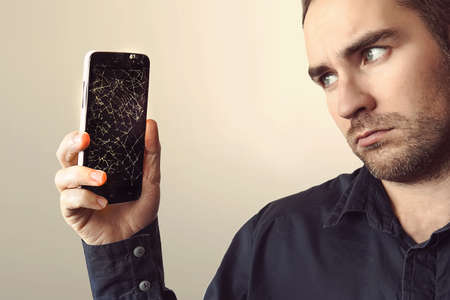 Young businessman with broken smartphone. a sad look. guy was upset about breaking his phone. Shattered phone displayの写真素材