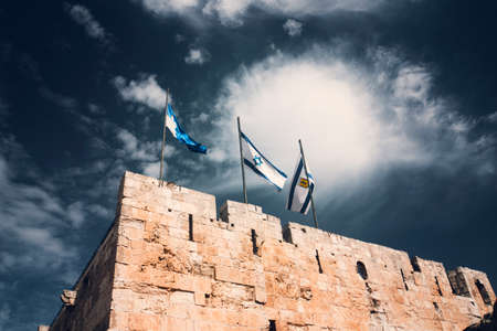 Israel and Jerusalem flags on Jerusalem old city walls against the blue sky with white clouds in the Sunny summer light.の写真素材