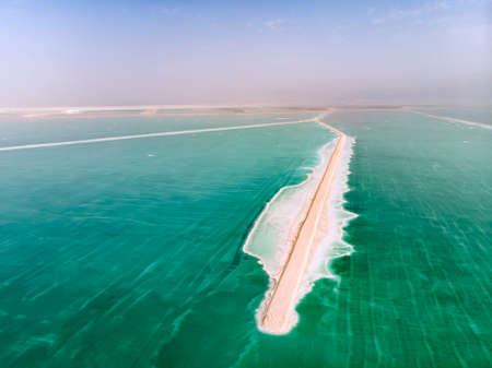 The southern part of the Dead Sea, is divided into pools from which extract minerals. The rocky shore is covered with white salt crystals washed by the blue waters of the dead sea.の写真素材