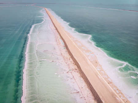 Road on Dead Sea surface. The southern part of the Dead Sea, is divided into pools from which extract minerals. shore is covered with white salt crystals washed by the blue waters of the dead sea.の写真素材