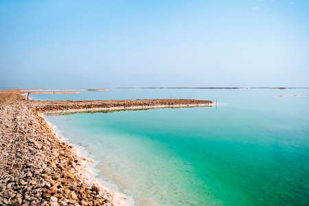 The southern part of the Dead Sea, is divided into pools from which extract minerals. The rocky shore is covered with white salt crystals washed by the blue waters of the dead sea.の写真素材