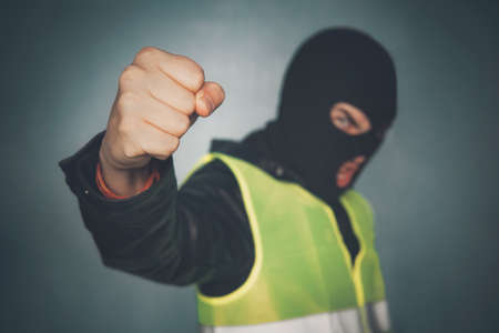 Rebellious protester in a mask shows his fist. Yellow Vest protest. street riots. French revolution. Angry thug bully threatening power. idea fighting poor proletarians against government and systemの写真素材