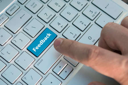 Computer key showing the word Feedback. Message on keyboard key, A male finger presses a color button on a gray silver keyboard of a modern laptop. Button with inscription close up.の写真素材