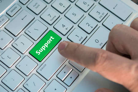 green support keyboard button. A male finger presses a color button on a gray silver keyboard of a modern laptop. Button with inscription close up.の写真素材