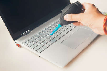 Closeup shot of female hand sweeping dust from laptop keyboard using air bulb.