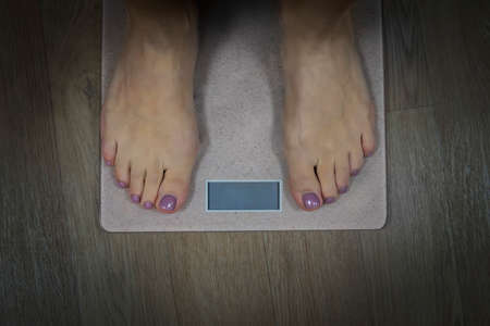 Diet and fitness concept. Close up to female bare feet with pedicure standing on scales with empty...