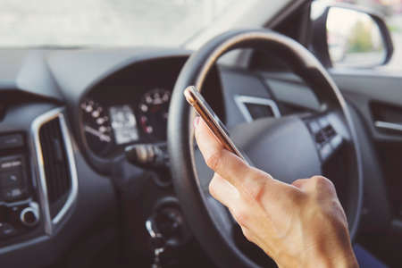Close up of female hand holding smatrphone and typing while driving. Woman texting message using...