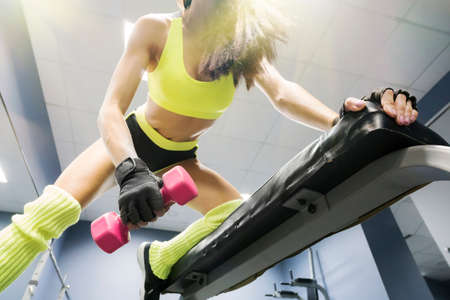 Strong young brunette woman doing push ups exercise with pink dumbbells. Fitness model doing intense training in the gym. Down-top view to sportswoman's workout. Upper body exercising in health clubの写真素材