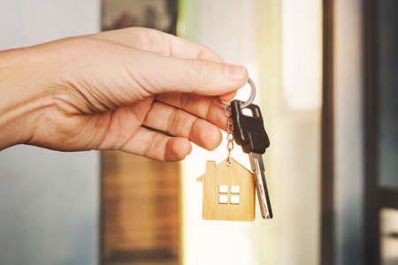 House key in male hand at apartment background. house key ring. Concept of moving in new living apartment. Symbol of purchasing house. Estate investment. Buy property. real estate transaction.の写真素材