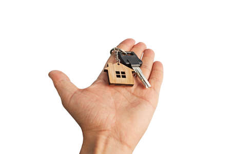 Isolated male hand holding in hand chrome key with wooden house tagged to key ring. Abstract illustration of hand handing over key with little house at white background. Purchasing dwelling concept.の写真素材
