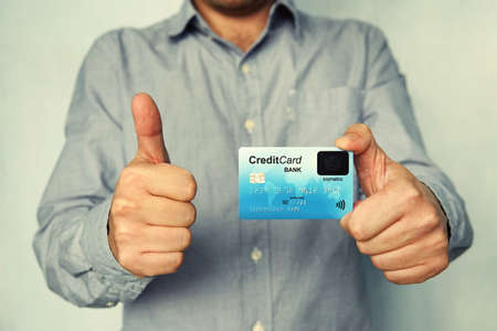Cropped shot of young man in shirt holding credit card with biometric technology and showing thumb up. Man is glad to use bank card of new type. Advantages of using banking. Biometric payment card.の写真素材