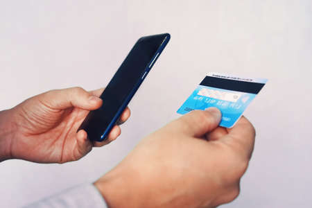 Online payment concept. Man using credit card with mobile phone at white background. Male hands holding smartphone with blank screen and reverse bank card. Person pays using mobile. Transaction.の写真素材