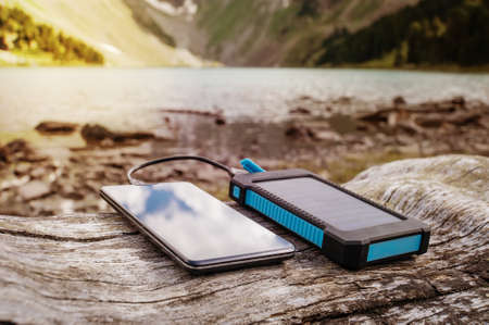 Portable solar panel for charging mobile devices lying on a log in the mountains where there is no electricityの写真素材