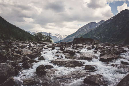 Clear river with rocks leads towards mountains. The river flows into the lakeの写真素材