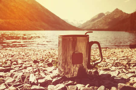 Cup of tea on wood with nature on background. Tourism and travel. Mag on the mountain lake on the background of beautiful sceneryの写真素材