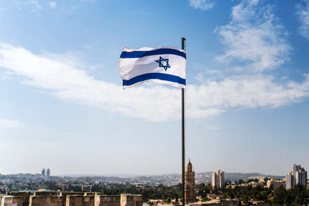 Israel flag flapping in the wind at good sunny day and old city backgroundの写真素材