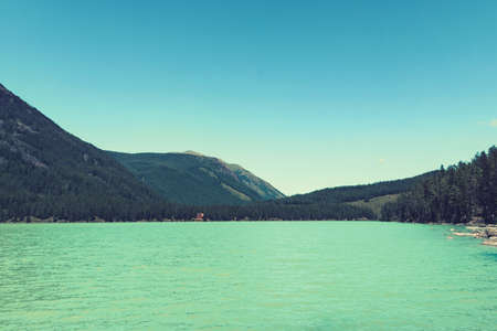 Beautiful landscape with turquoise lake, forest and mountains . Wooden house near the blue lake in dense forest among the trees. Tourist base in the Siberian taiga. Wooden frame house. Altai. Russiaの写真素材