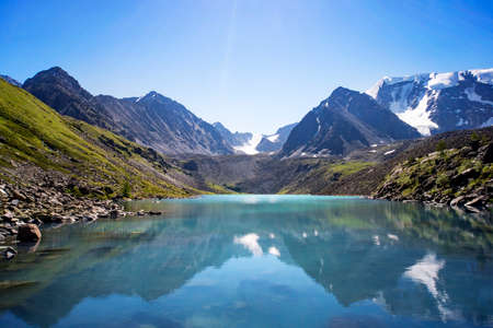 Russia, Altai, mountains. Beautiful blue lake Kucherla in the foreground against the snow-capped peaks of high mountains. Summer vacation in the mountains. reflection of mountains with snow-cappedの写真素材