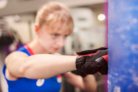 closeup shot of muscular woman learning to beat with fists indoors. practising hits. sparring .Punch the punching bag. The blonde sportswoman trains hand-to-hand combat.の写真素材
