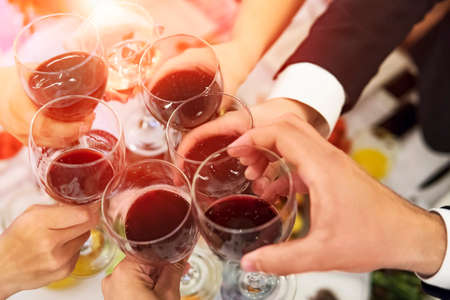 Male and female hands with filled glasses of wine above the restaurant tabletop. Drinking toasts and...
