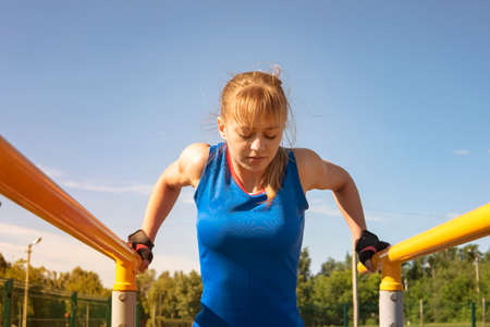 A sports girl is training in the park on the horizontal bars