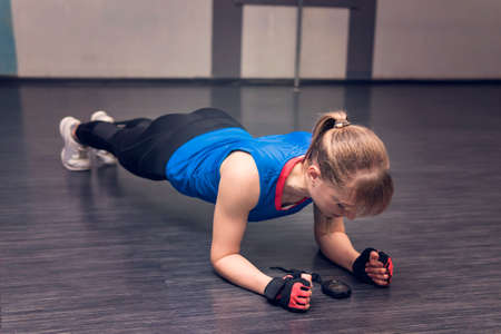 A girl with white hair standing on his hands. Endurance training. The athlete looks at the timer or stopwatch. Exercise for time.. beautiful sporty young woman doing push ups in fitness studioの写真素材
