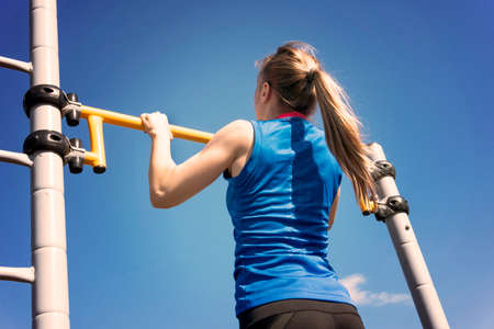 young athletic fitness woman working out at outdoor gym doing pull ups at sunrise.の写真素材