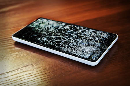 Modern frameless Smartphone with broken screen on the wooden tableの写真素材