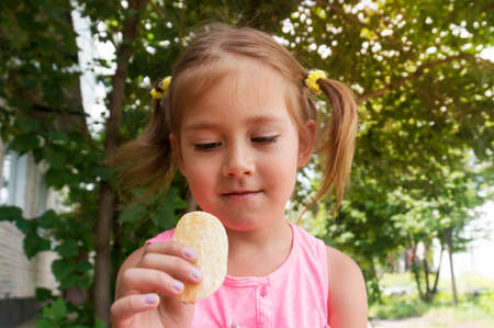 pretty girl having fun outdoors. Baby puts potato chips in his mouth. Bad food. Jung food. Fried potatoes of the correct form.の写真素材