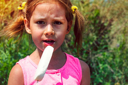 Child eating ice cream. Kids play outdoors enjoying sweet snack on a hot summer day. Children eat icecream. Toddler kid playing in the garden. Little girl with vanilla iceの写真素材