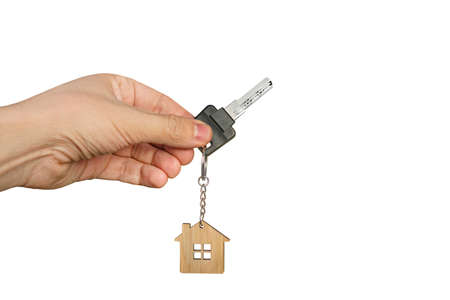 Close up of male hand at white background holding key with wooden house key ring. Concept of...